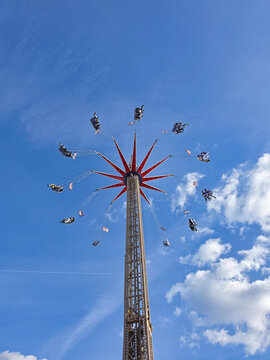 Hanover, Lower Saxony, Germany - 06 April 2026: View of a tall Star Flyer swing ride spinning against a clear blue sky with fluffy white clouds at a fairground.