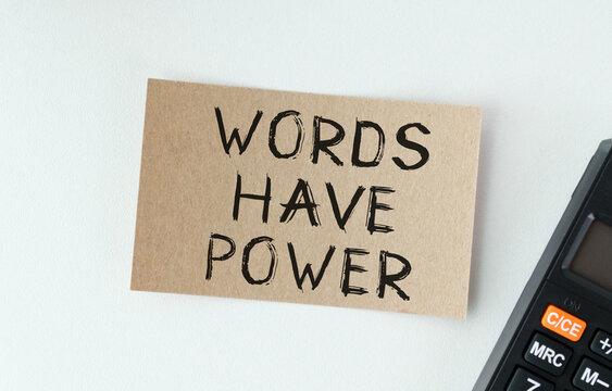 Brown card with bold handwritten words: WORDS HAVE POWER. Black calculator rests beside the card.