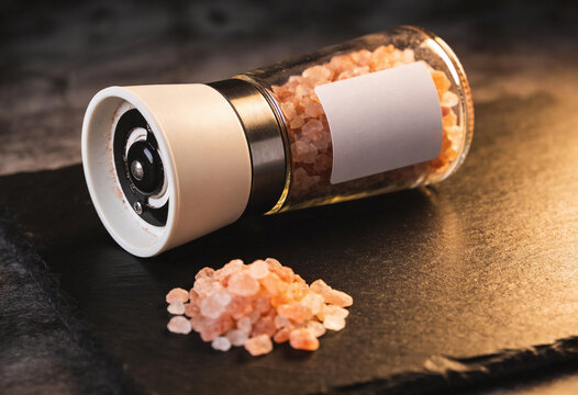 Pink himalayan salt grinder mill on slate board, rock salt crystals, seasoning spice, gourmet cooking ingredient, salt shaker, food seasoning, kitchen condiment, natural mineral salt, culinary spice.