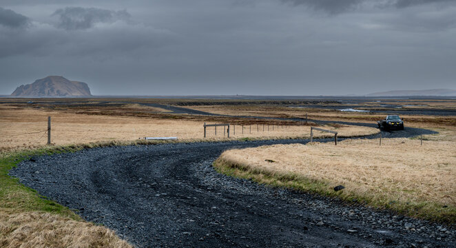 Black suv driving on F249 winding gravel road across a desolate icelandic volcanic valley distant mountains under a cloudy sky. Porsmork Road, rugged landscape, Thorsmork Road
