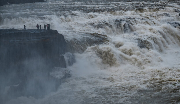 Tourists standing on a cliff at gullfoss, experiencing the immense power of the golden waterfall and glacial river hvita. Iceland golden circle tourism route