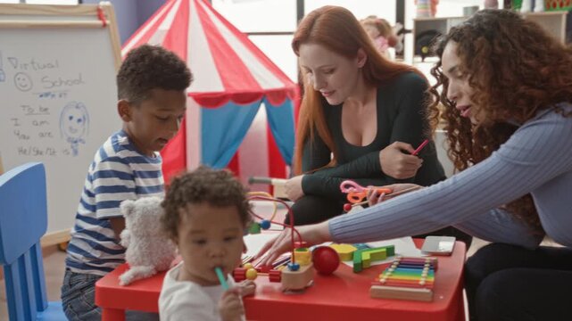 Woman leans in and guides children playing with a wooden xylophone, bead maze and blocks at a small red table in a building; nurturing learning.