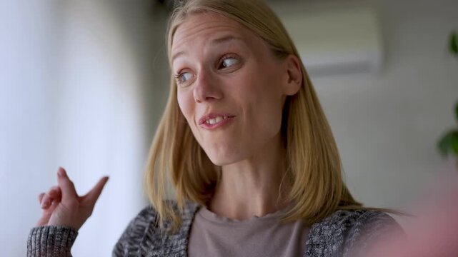Happy young woman talking during an online video conversation from a bright home interior, expressing warmth, connection, friendship, and authentic everyday communication