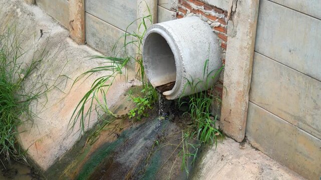 Concrete drainage pipe discharging wastewater into an open canal, showing environmental pollution and urban infrastructure issues in a residential area