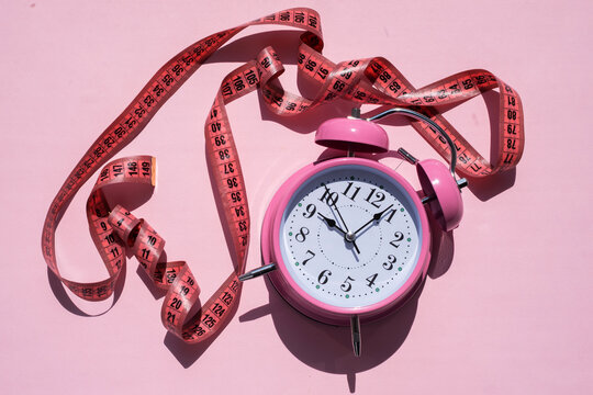 Pink alarm clock with a measuring tape for weight loss and intermittent fasting concept