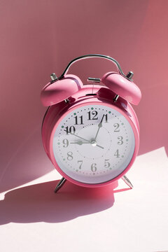Pink alarm clock with hard shadows for morning wakeup and time management concept