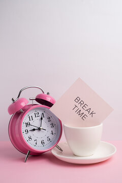 Pink alarm clock in a coffee cup with a Break Time note for work-life balance concept