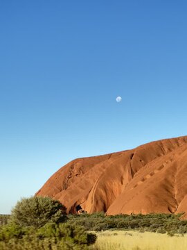 Red Uluru rock monolith under blue sky with moon in outback