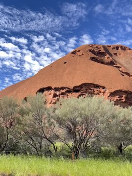 Textured red sandstone cliff of Uluru under cloudy blue sky