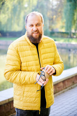 Man by pond examines headphones. Man inspecting headphone cable by tranquil pond. Man carefully...