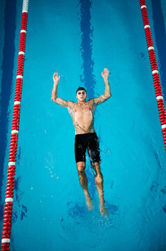 Swimmer floating on back in pool. Male athlete in swim cap and goggles practicing backstroke position, relaxed body, top view in indoor swimming pool lane