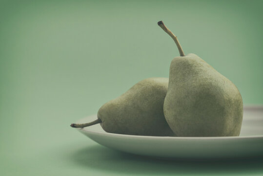 Close-up of Two green pears on a plate in front of a green background