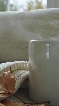 Vertical video: Rising wisp causing white mug sending steam from heat on sofa by window, knit throw