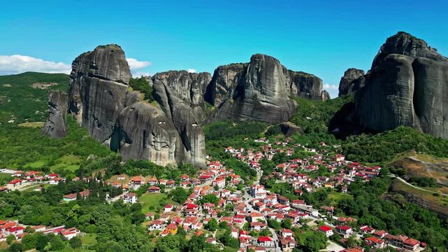 Aerial view of the towering rock formations of Meteora with a village nestled below under a clear blue sky in Greece.