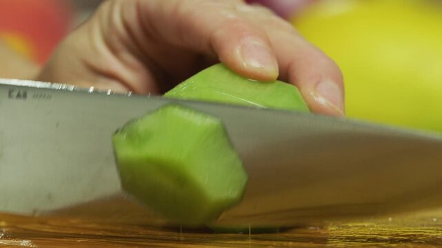 Large knife slicing up skin-less kiwi on chopping board - closeup, slow motion