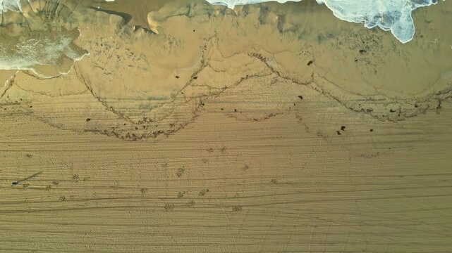 Aerial view of sandy beach with tire tracks and ocean waves in Los Angeles, California, United States.
