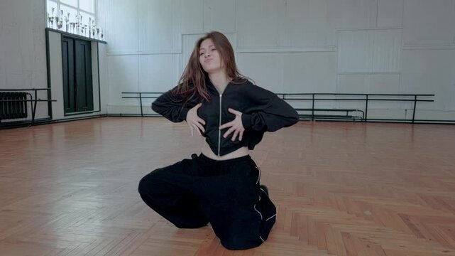 A young  girl is dancing jazz funk inside a studio.She performs a dynamic and sharp modern choreography.The dancer is wearing a black stylish sport outfit.