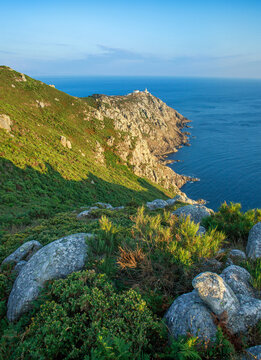 Breathtaking landscape a headland and lighthouse on the slope of rocky cliff, on the blue ocean and sky