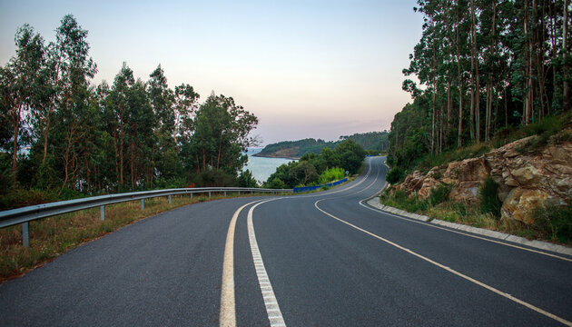 Evening landscape, paved road, highway, amidst forest on hill overlooking the seacoast, set against a twilight sky