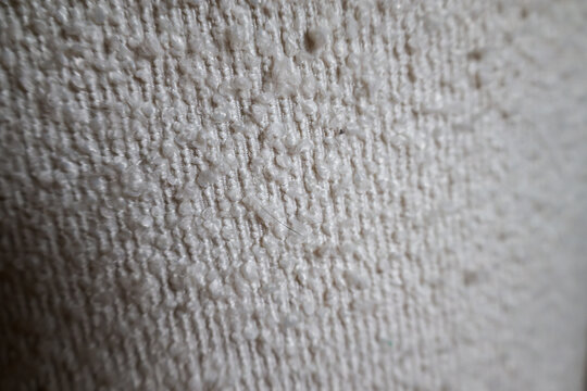 Detailed macro view of white cream textured fabric with soft nubby boucle weave and looped fiber structure. Natural textile surface showing plush raised texture and neutral tone. Cozy soft background.