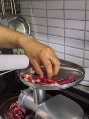 Hand placing pieces of raw meat into electric meat grinder while making homemade minced meat in kitchen. © Anastassiya 
