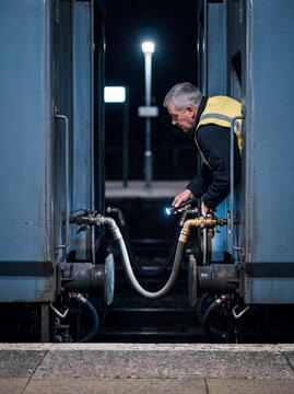 Bahntechniker pr&uuml;ft Bremsschlauch zwischen Waggons bei Nacht