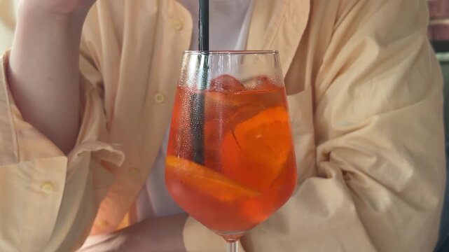 Glass of Aperol spritz cocktail with black straw on restaurant table, refreshing orange summer drink for outdoor cafe, social dining and relaxed evening atmosphere