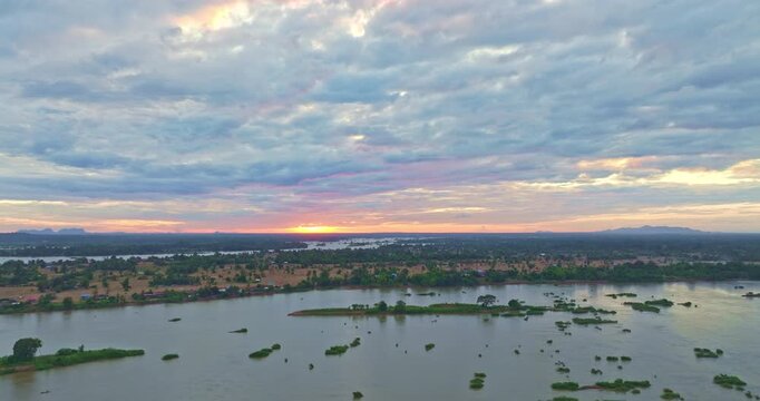 A panoramic drone shot of the Mekong River at sunset over Si Phan Don, featuring the iconic Khone Phapheng Waterfall. Rich colors, textured clouds, and flowing rapids create a visually striking ideal