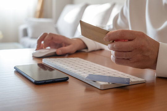 Person holding a credit card while using a computer mouse and keyboard for e-commerce, banking, or digital subscriptions, indicating secure online payment processing