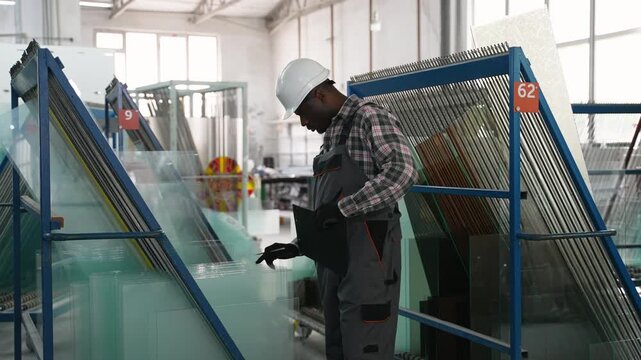 African American factory worker checking glass sheets with tablet