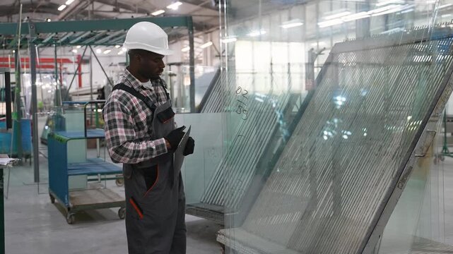 African American male worker inspecting glass panels in a factory
