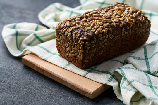 loaf of freshly baked wholemeal rye bread with sunflower seeds on dark kitchen table, selective focus.