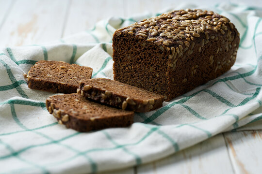 loaf of freshly baked wholemeal rye bread with sunflower seeds on white kitchen table.