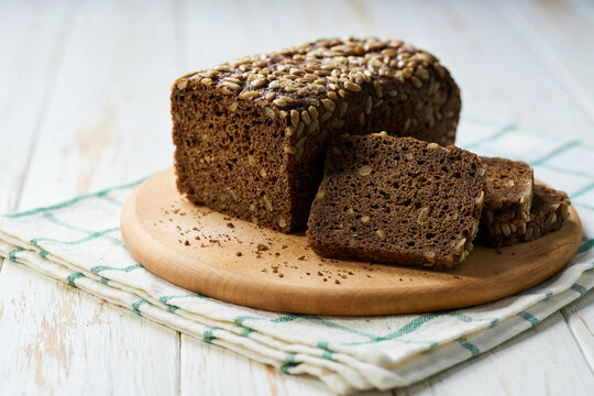 loaf of freshly baked wholemeal rye bread with sunflower seeds on white kitchen table.
