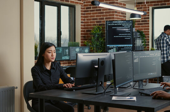 Programmer holding a clipboard sits near a colleague writing code as database admins work on big data, machine learning software and a shared development project.