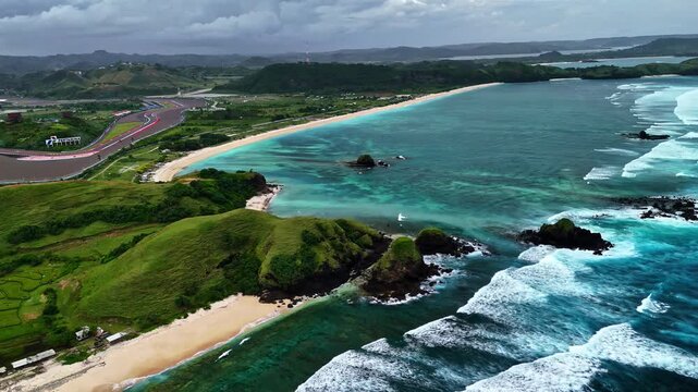 Aerial view of the Mandalika International Street Circuit coastline with turquoise water, waves, and green hills in Lombok, Indonesia.