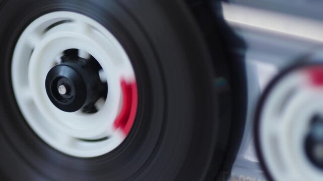 Macro shot of a spinning cassette tape reel inside an analog audio recorder deck. Retro sound equipment playing music in close-up detail.
