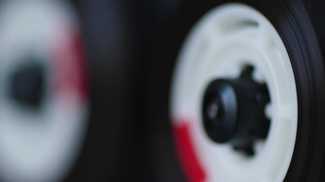 Close-up of two rotating cassette reels with magnetic tape on a recorder deck. Vintage audio equipment plays sound in a shallow depth of field macro view.