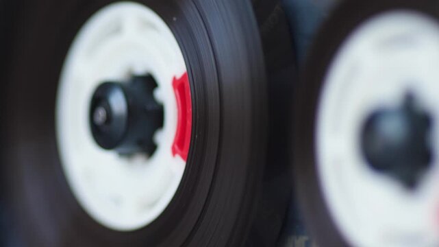Close-up of a spinning cassette reel with magnetic tape on a retro tape recorder. Analog audio equipment plays sound in a macro view with a blurred background.