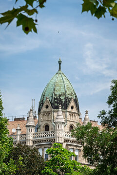Green copper dome and spires of the Sv&aacute;b House commercial and apartment building seen through tree branches in Budapest, Hungary