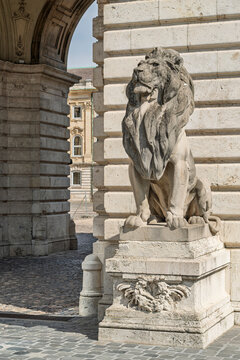 Seated stone lion statue on a pedestal guarding a ribbed stone archway at the entrance to Buda Castle in Budapest, Hungary