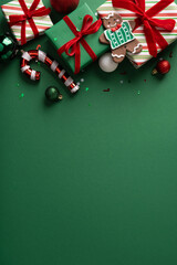 Obraz premium Christmas gifts with gingerbread cookie, red ribbons and ornaments on green vertical background for Merry Happy New Year