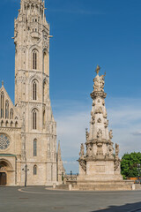 Fototapeta premium Tall Gothic tower of Matthias Church beside the Holy Trinity Statue on an empty plaza in Budapest, Hungary