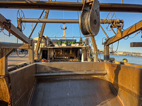 View of heavy mechanical winches and equipment on a commercial fishing boat docked in a harbor on a clear day