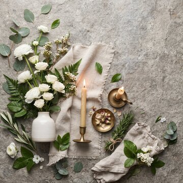 A beautifully arranged composition of white roses, greenery, and burning candles rests on a textured stone surface, evoking a sense of elegant tranquility and natural beauty.