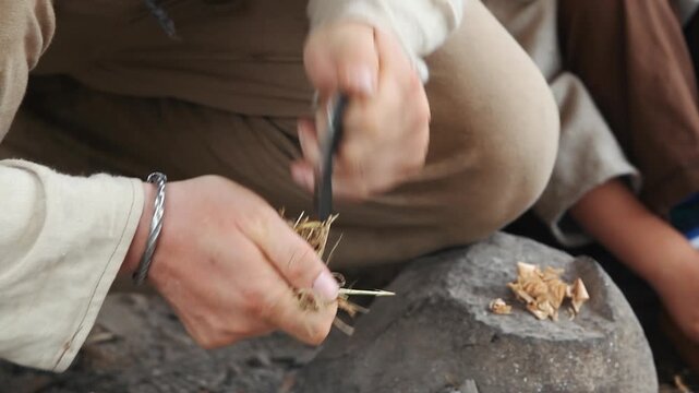 Close-up of hands using a traditional flint and steel to strike sparks onto dry grass tinder. Historical reenactment, bushcraft, and primitive fire starting concept.