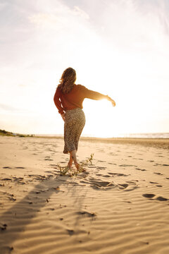 A woman strolls along a sandy beach at sunset. The young woman feels free, enjoying herself and having fun on the seashore. Concept of nature, beauty, and freedom.