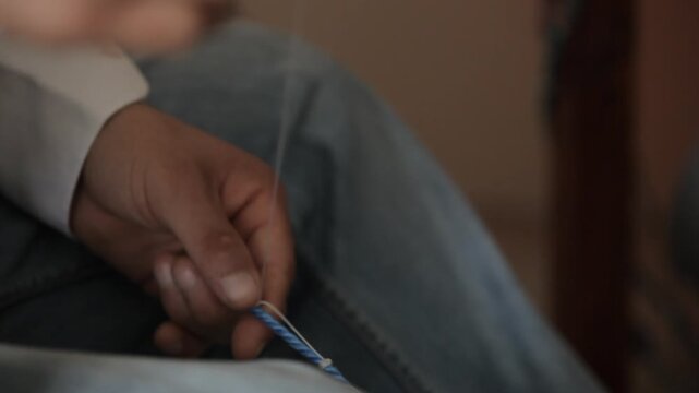 Close-up of hands using a traditional netting needle to weave and knot a blue rope. Fishing net making, traditional maritime craftsmanship, and handmade skill concept.