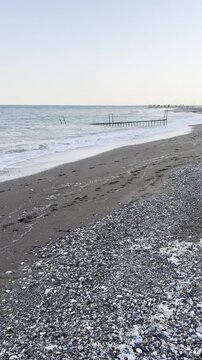 Hafif dalgaların vurduğu taşlık bir sahilde dağılmış plastik atıklar, doğal kıyı g&uuml;zelliği ile &ccedil;evre kirliliği arasındaki zıtlığı g&ouml;steriyor.