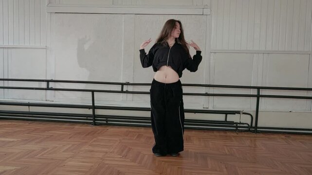 A beautiful girl energetically dances jazz funk, waves her hair up and down, smiles.The dance rehearsal takes place in a spacious studio.A double ballet barre is attached to the wall.